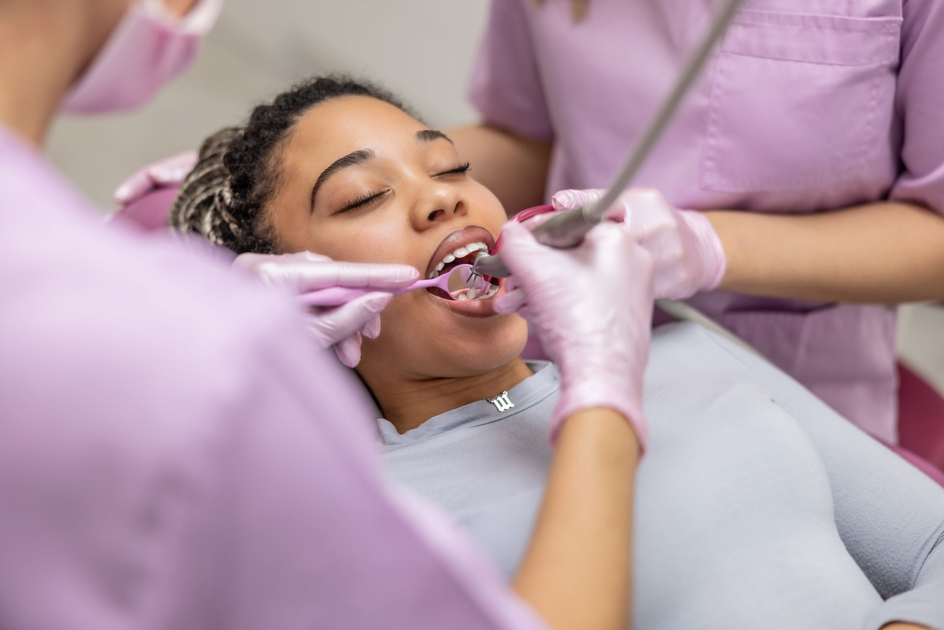 A female dentist drills a young woman's tooth, and her dental assistant suctions saliva