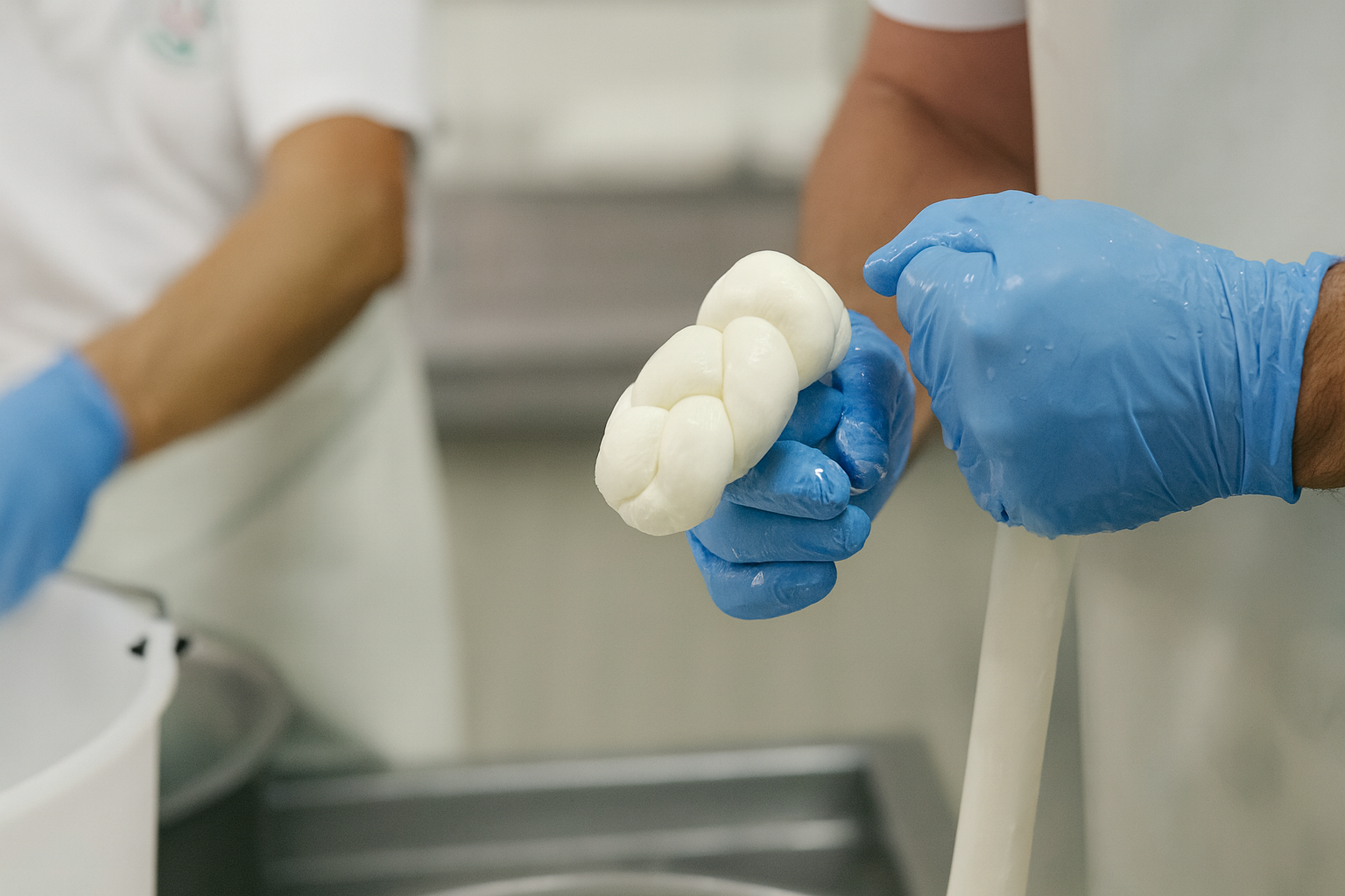 Mani con guanti blu che intrecciano la mozzarella fresca.
