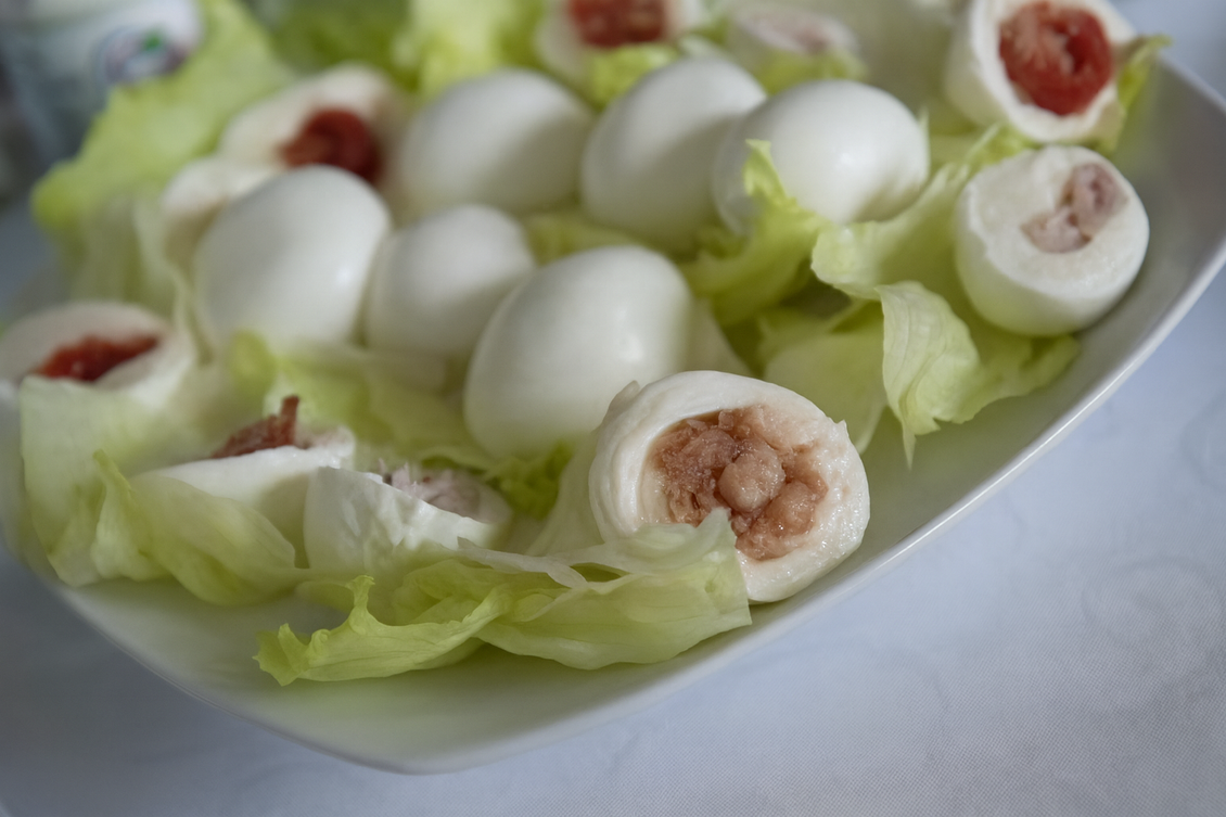 Palline di mozzarella bianca, alcune tagliate a metà per rivelare il ripieno, disposte su lattuga in un piatto bianco.