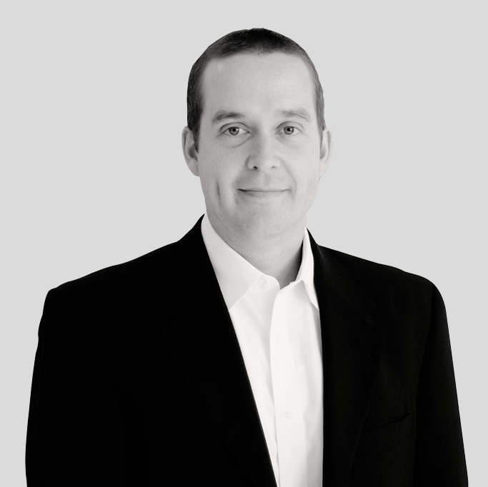 A man in a suit and white shirt is smiling in a black and white photo.