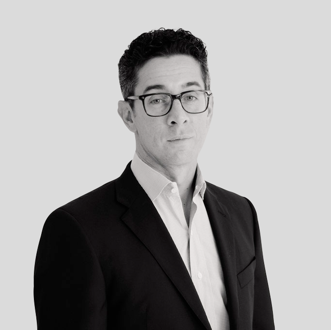 A man in a suit and glasses is standing in front of a white background.