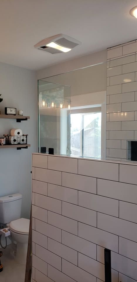 A bathroom with white tiles , a toilet , and a large mirror.