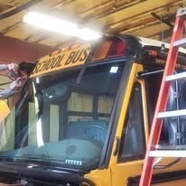 A school bus is being repaired in a garage with a ladder.