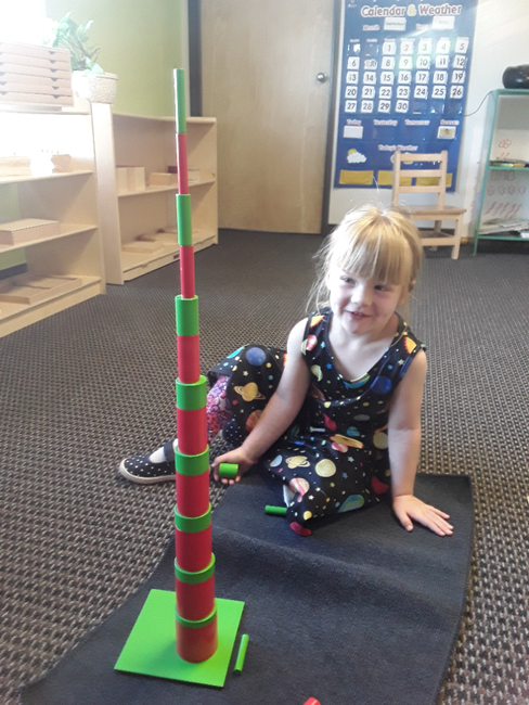 A little girl is sitting on the floor playing with a montessori tower