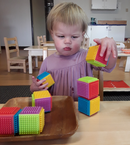 A little girl is playing with colorful montessori blocks on a table