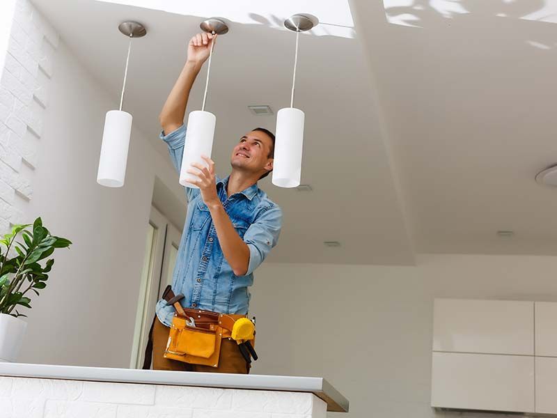A man is hanging a light from the ceiling in a kitchen.