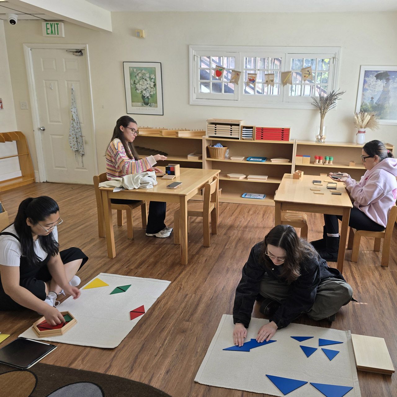 Adult students in an AMS training program practice with Montessori geometric blue triangles on floor mats.