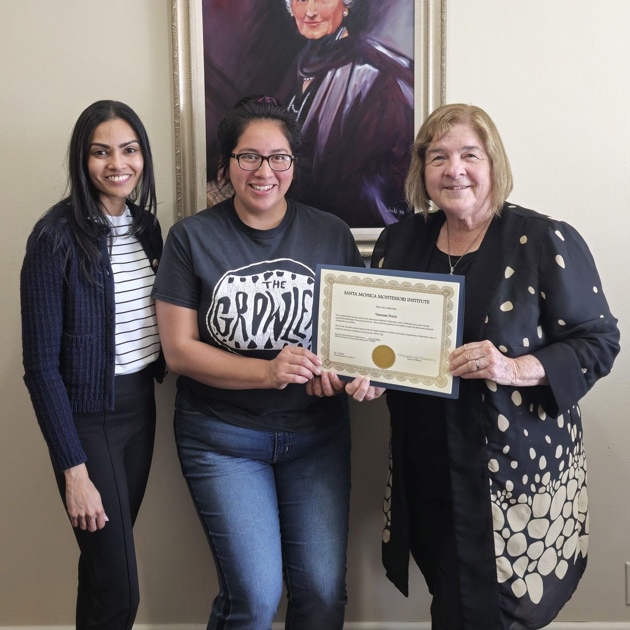 A student proudly displays her Santa Monica Montessori Institute certificate alongside faculty members.