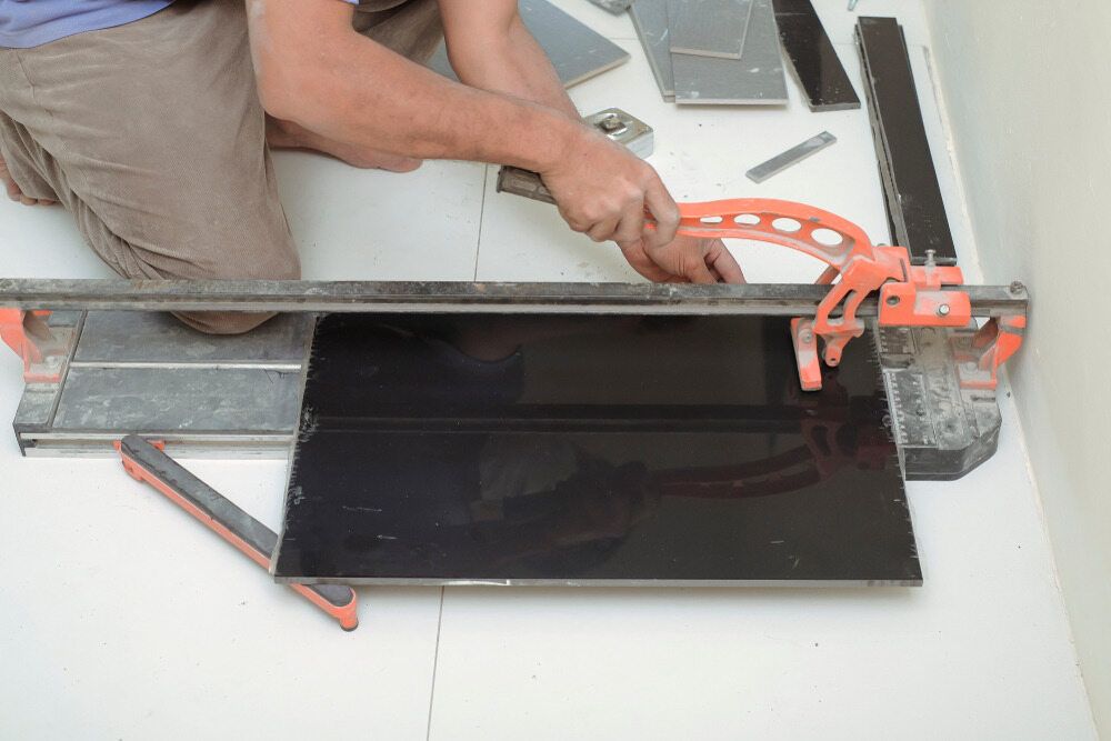 A Man is Cutting a Tile With a Tile Cutter — Mark's Flooring & Handyman Services in Wyong, NSW