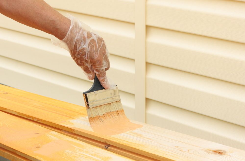 A Person is Painting a Piece of Wood With a Brush — Mark's Flooring & Handyman Services in Wyong, NSW