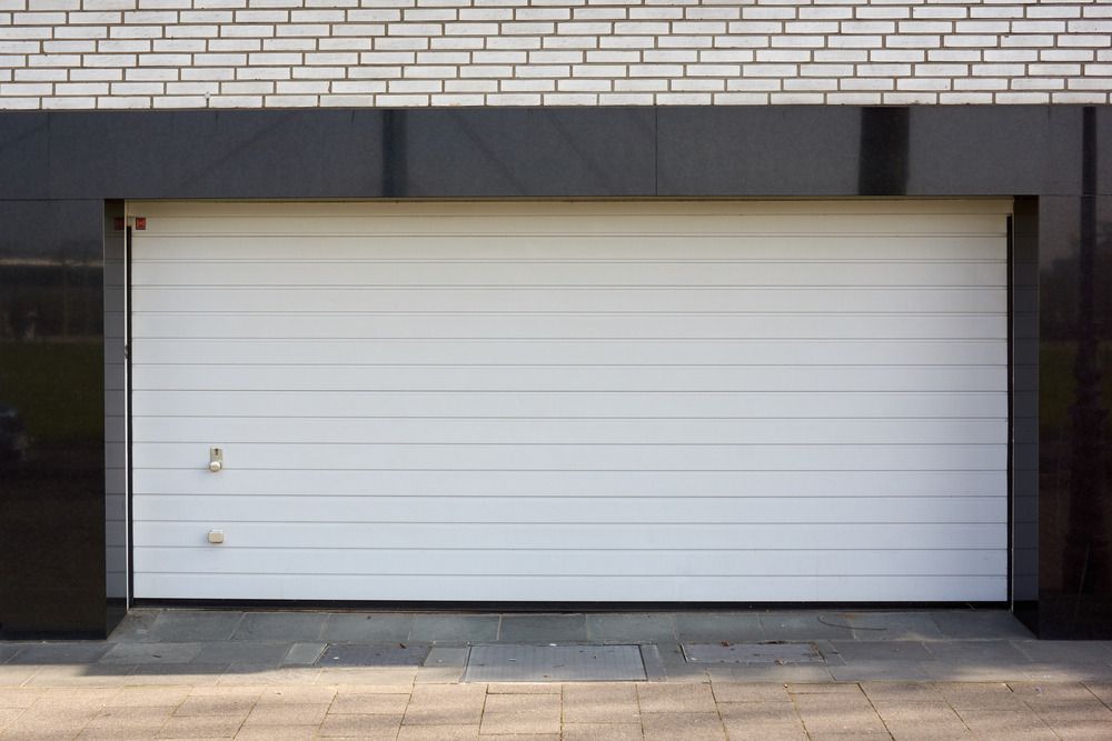 A White Garage Door is Open in Front of a Brick Building — Mark's Flooring & Handyman Services in Wyong, NSW