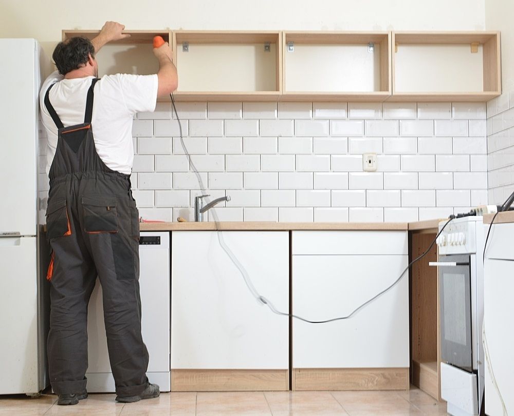 A Man is Working on a Kitchen With a Drill — Mark's Flooring & Handyman Services in Doyalson, NSW