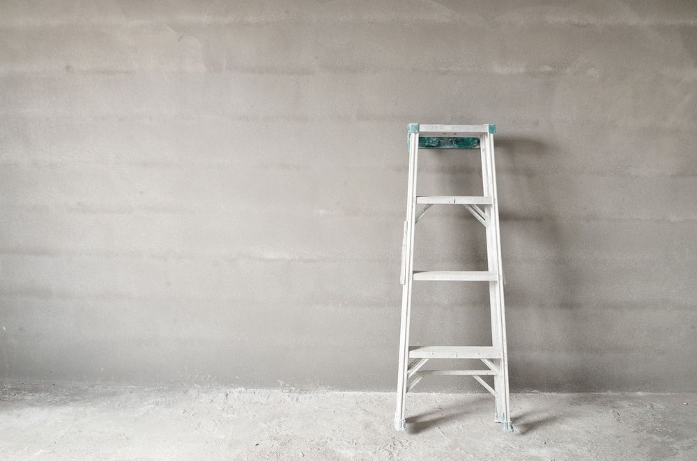 A White Ladder is Leaning Against a Gray Wall in an Empty Room — Mark's Flooring & Handyman Services in Wyong, NSW