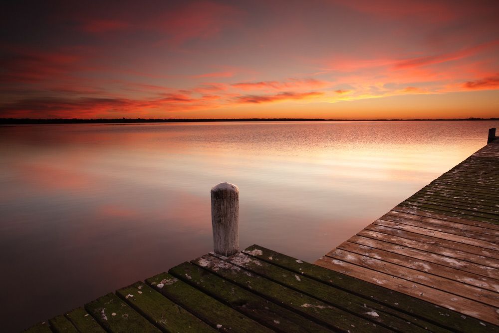 A Wooden Dock Overlooking a Lake at Sunset — Mark's Flooring & Handyman Services in Berkeley Vale, NSW