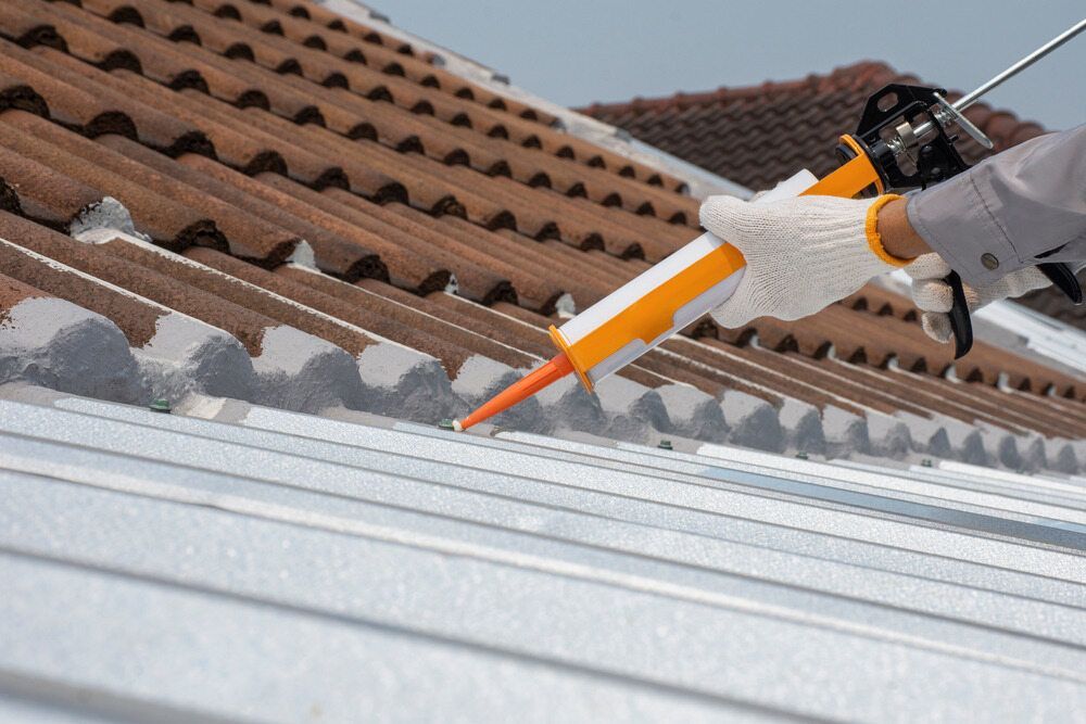 A Person is Applying Sealant to the Roof of a Building — Mark's Flooring & Handyman Services in Berkeley Vale, NSW