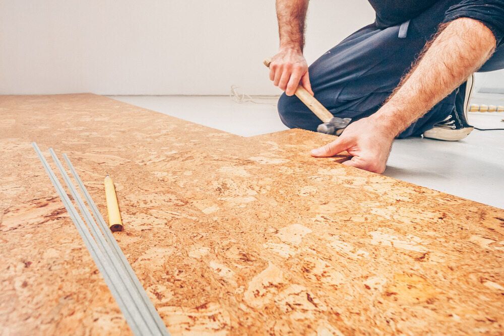 A Man is Installing a Cork Floor With a Hammer — Mark's Flooring & Handyman Services in Berkeley Vale, NSW