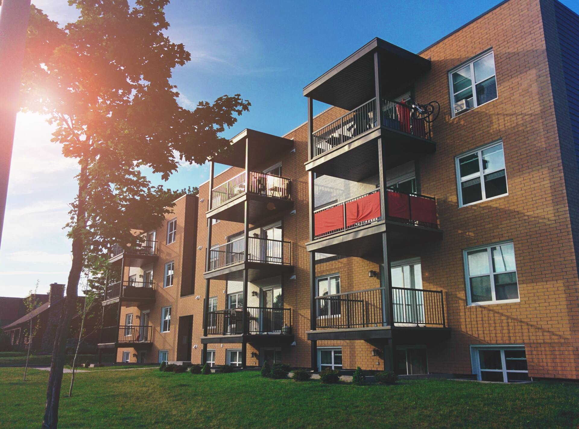 A brick apartment building with balconies and a tree in front of it