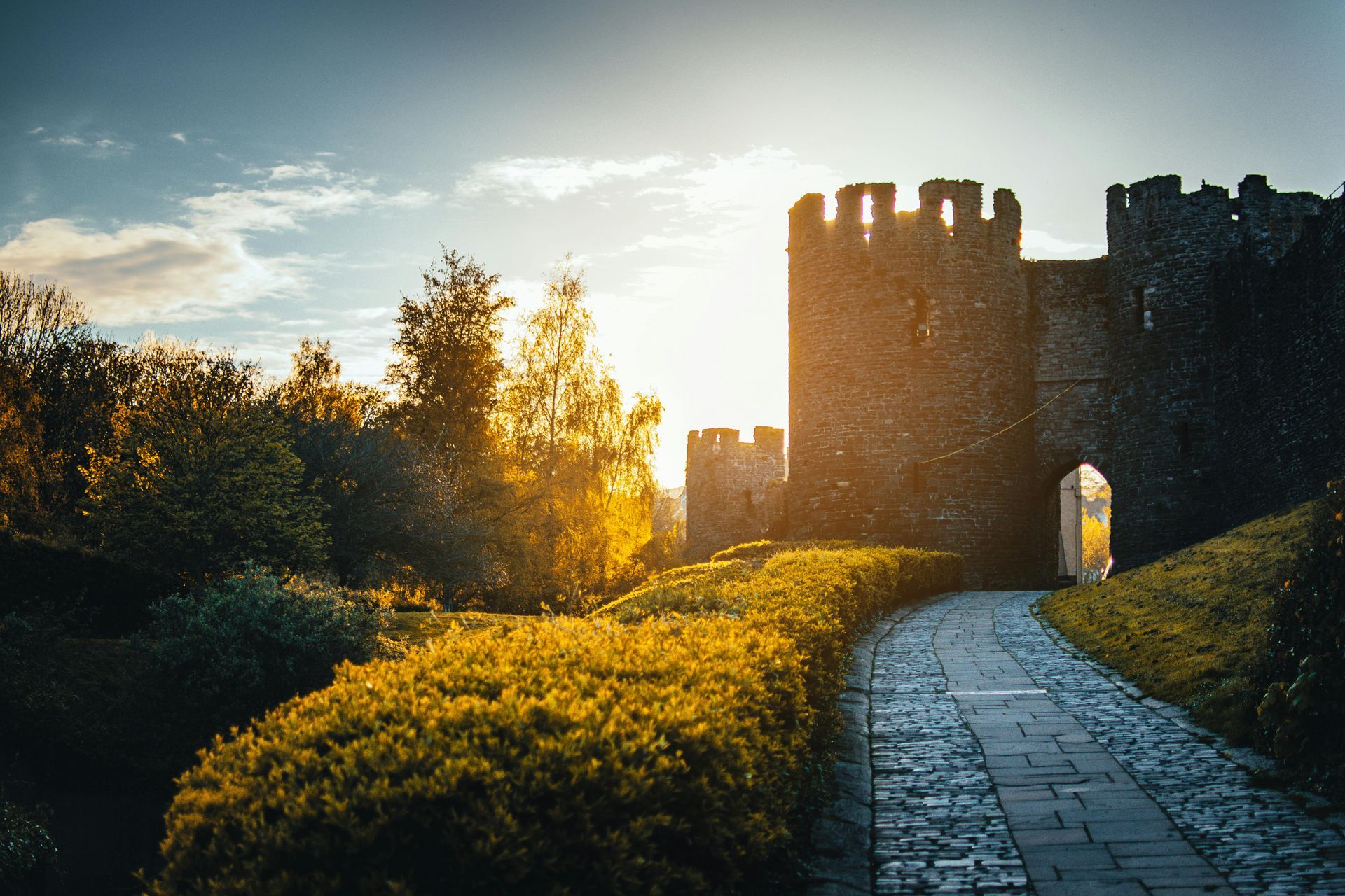 Stone castle entrance with a path leading to the gate, bathed in warm sunlight.