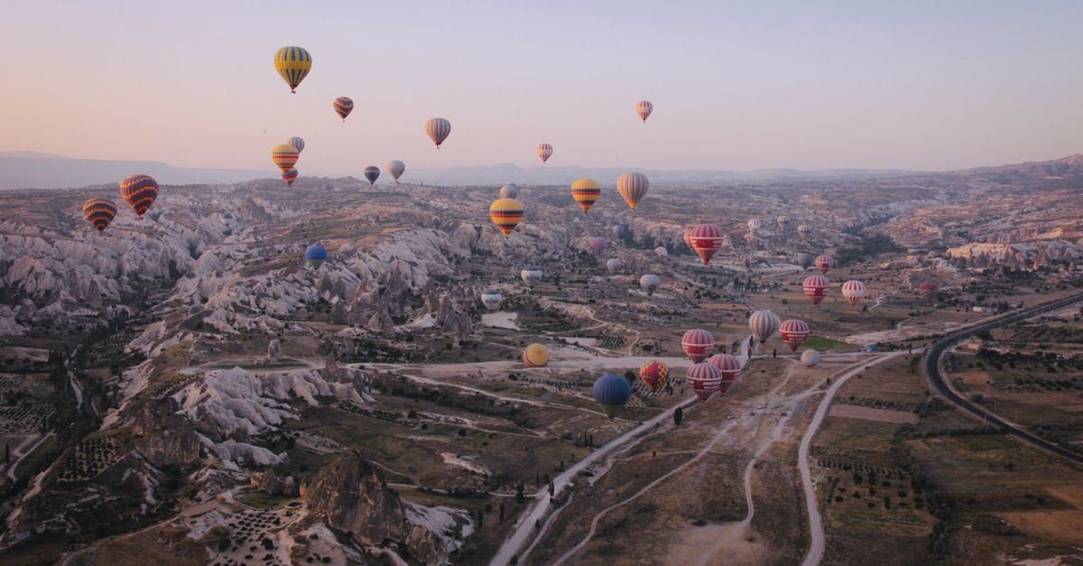 Hot air balloons fill the sky over a rocky landscape, bathed in soft sunset hues.