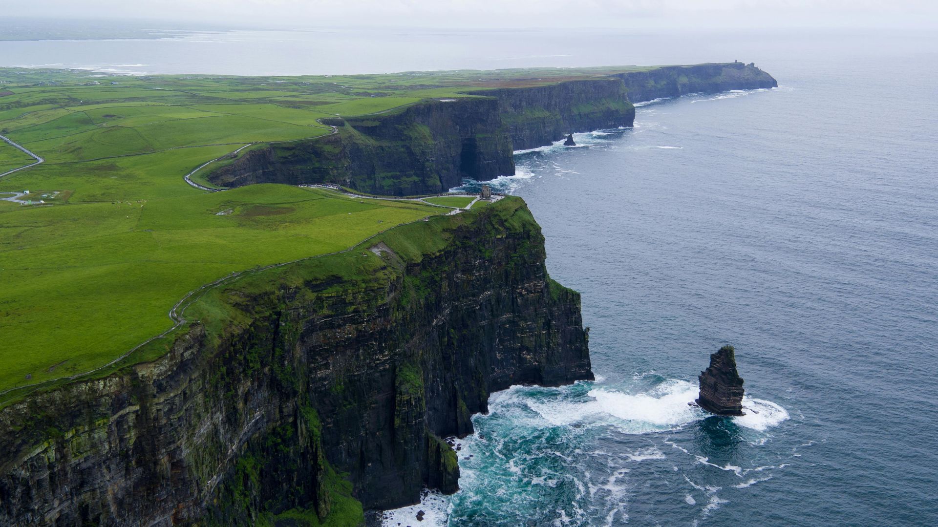 Cliffs of Moher, Ireland, with green grass on top, rugged cliffs, and crashing waves.