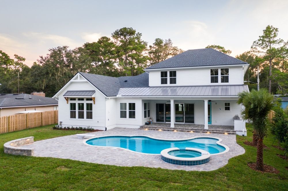 Two-story white house with pool and patio, surrounded by trees and green grass.