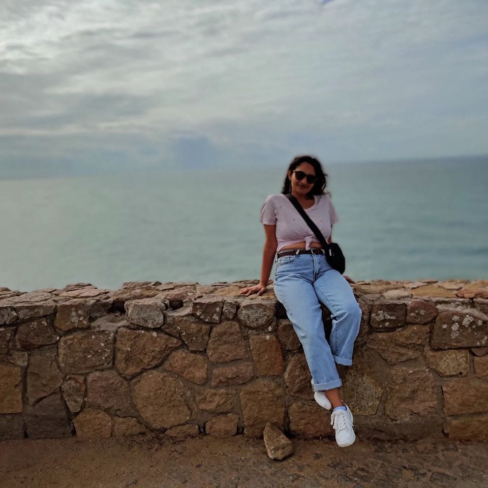 Anam Ahmed, freelance copywriter, on a trip to Portugal, sitting on a coastal wall