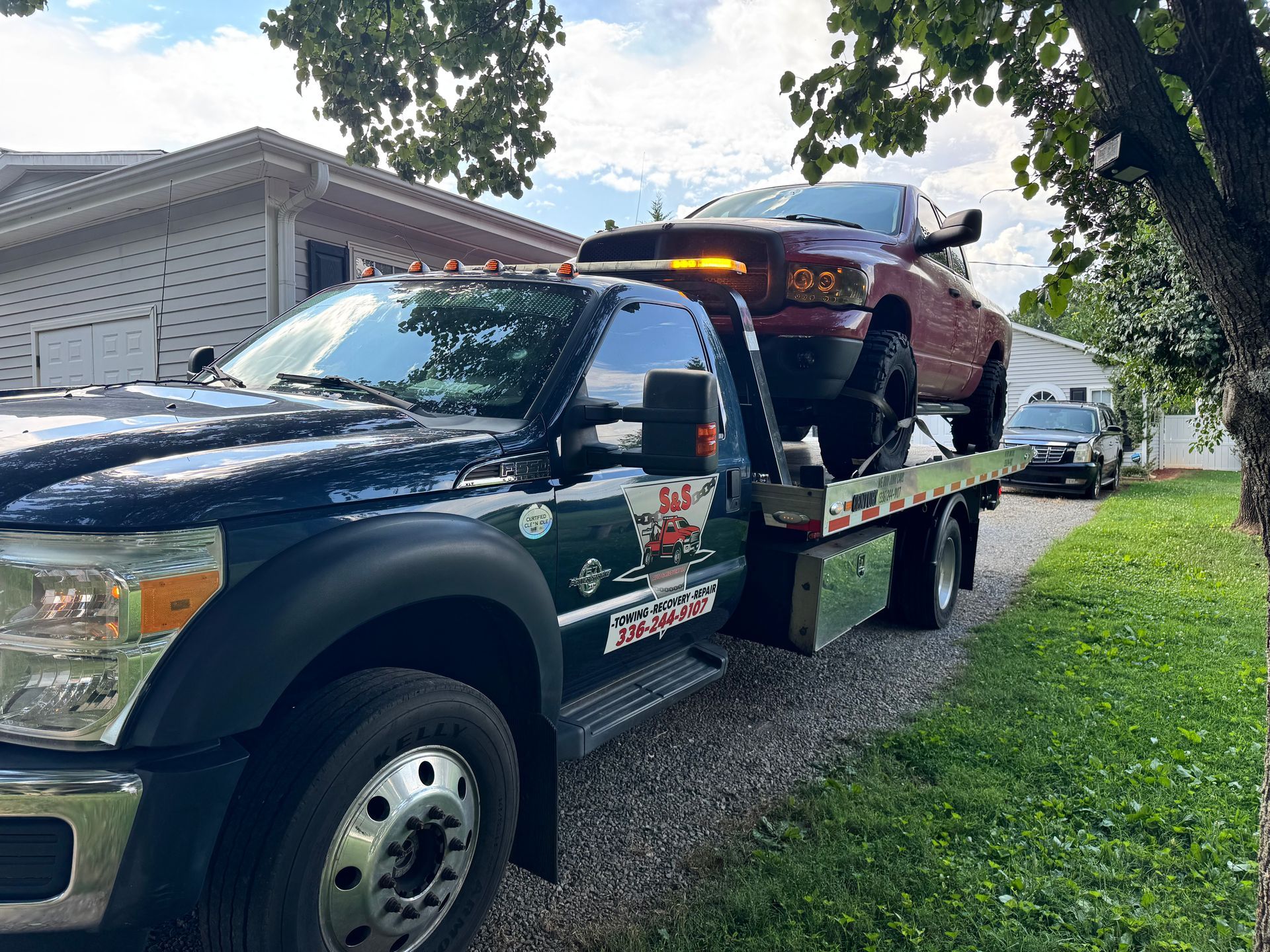 Tow truck carrying a red pickup truck on a residential street.