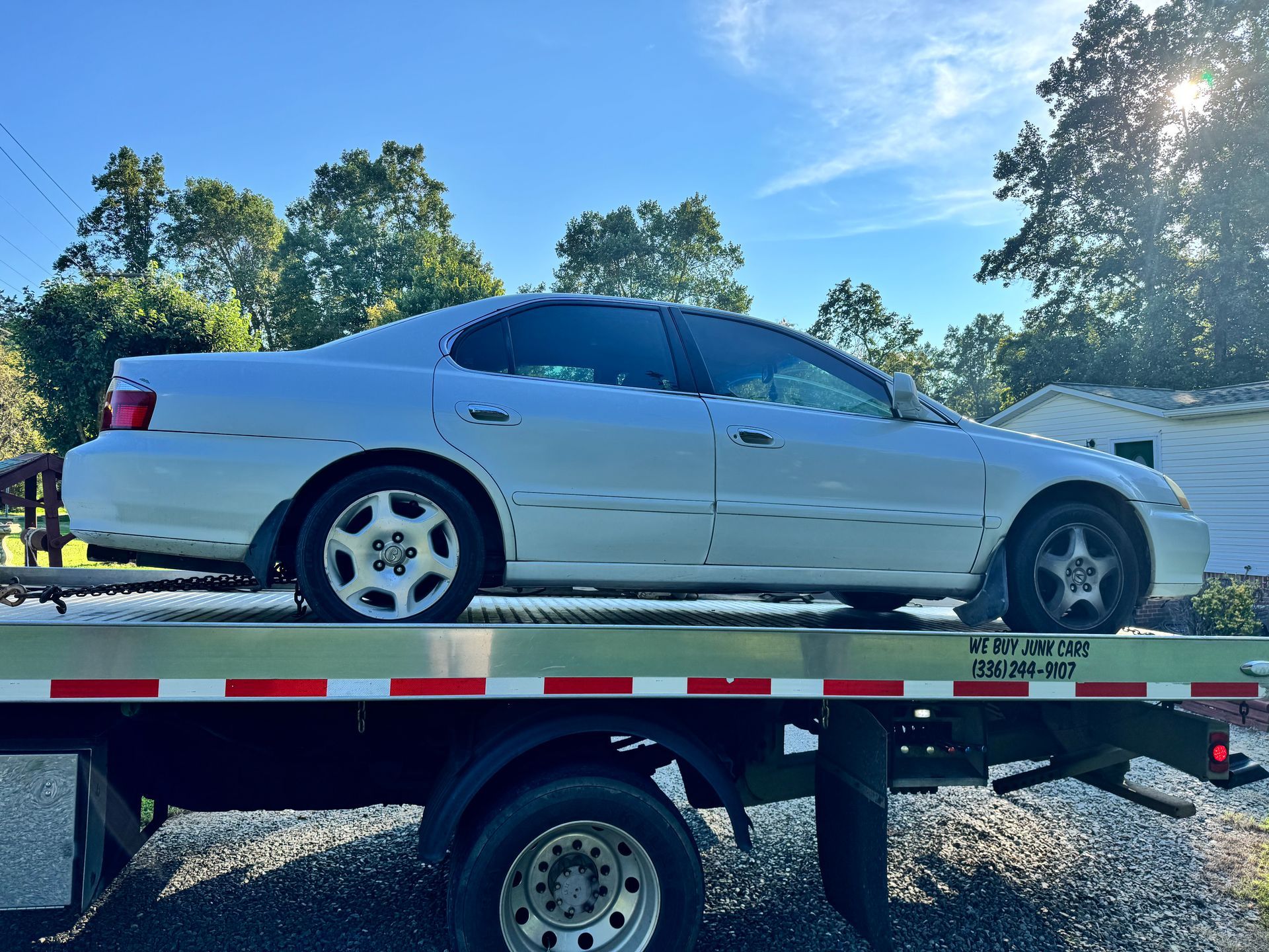 Silver sedan on a tow truck; sunny outdoor scene.