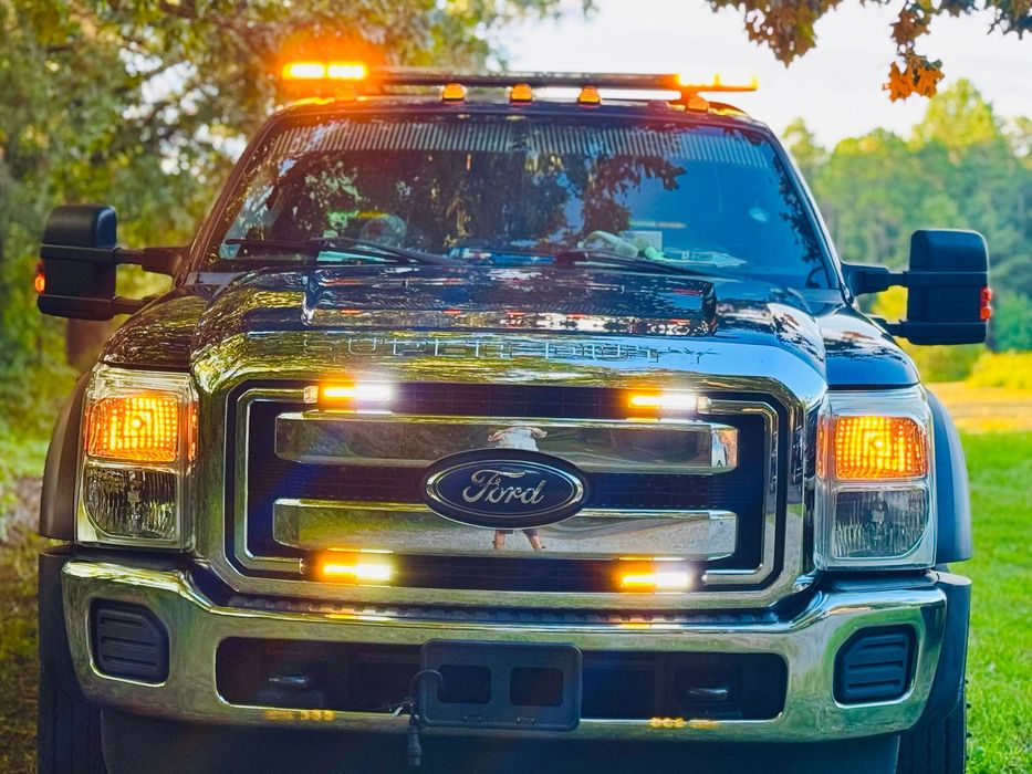 Black Ford truck with flashing amber and white lights, parked outdoors.