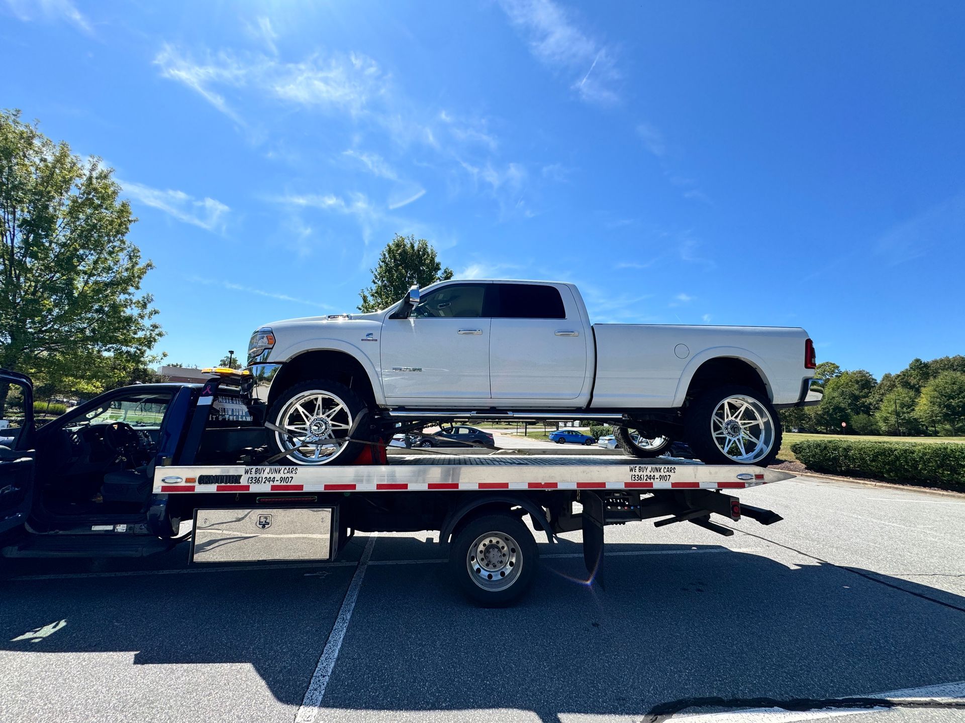 White pickup truck on a tow truck, parked outside on a sunny day.