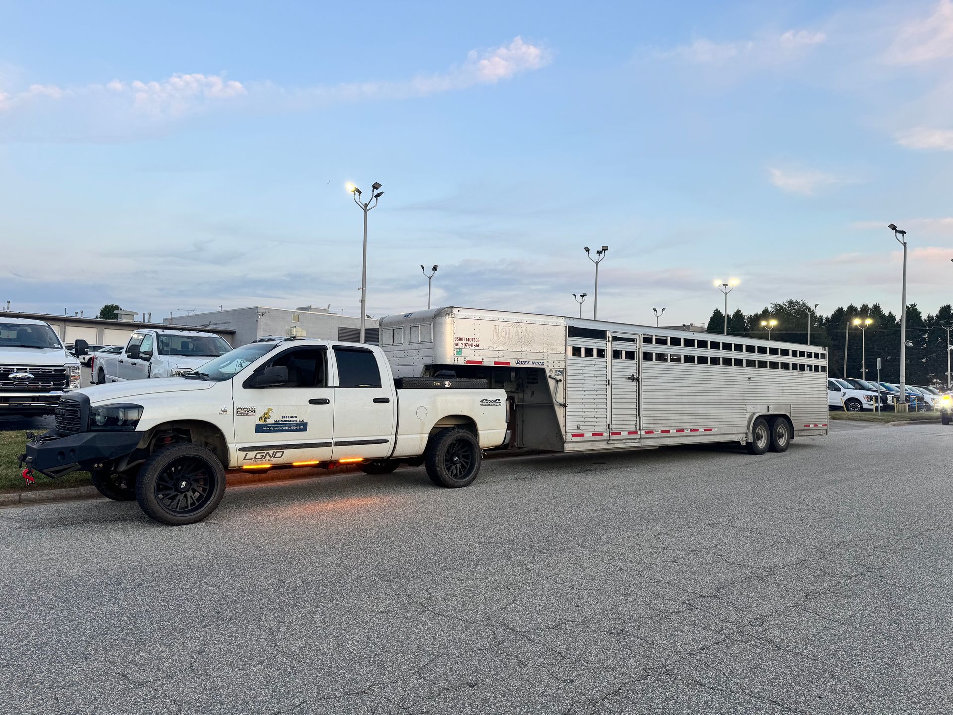 White pickup truck towing a livestock trailer parked in a lot, blue sky.
