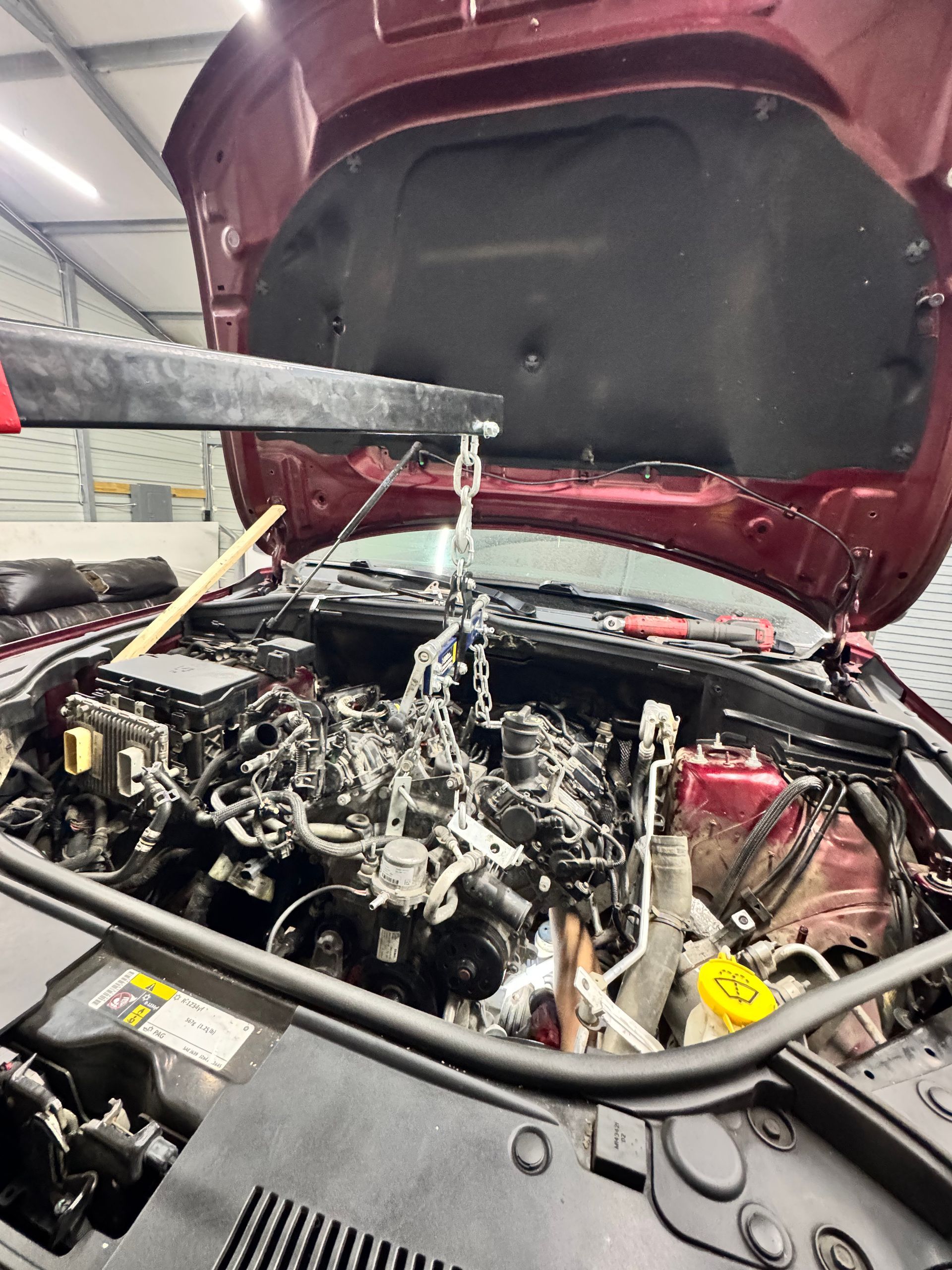 Car engine being lifted out, red vehicle, open hood, shop setting.