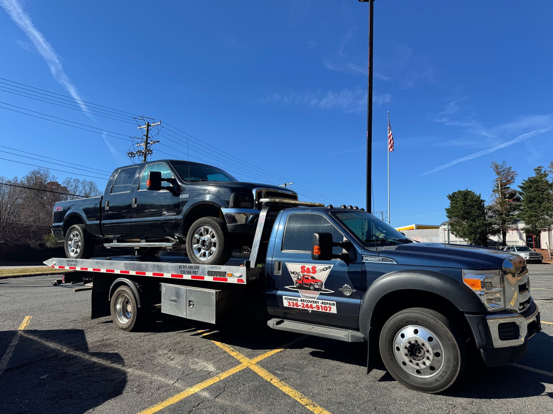 Tow truck carrying a black pickup truck on a sunny day.