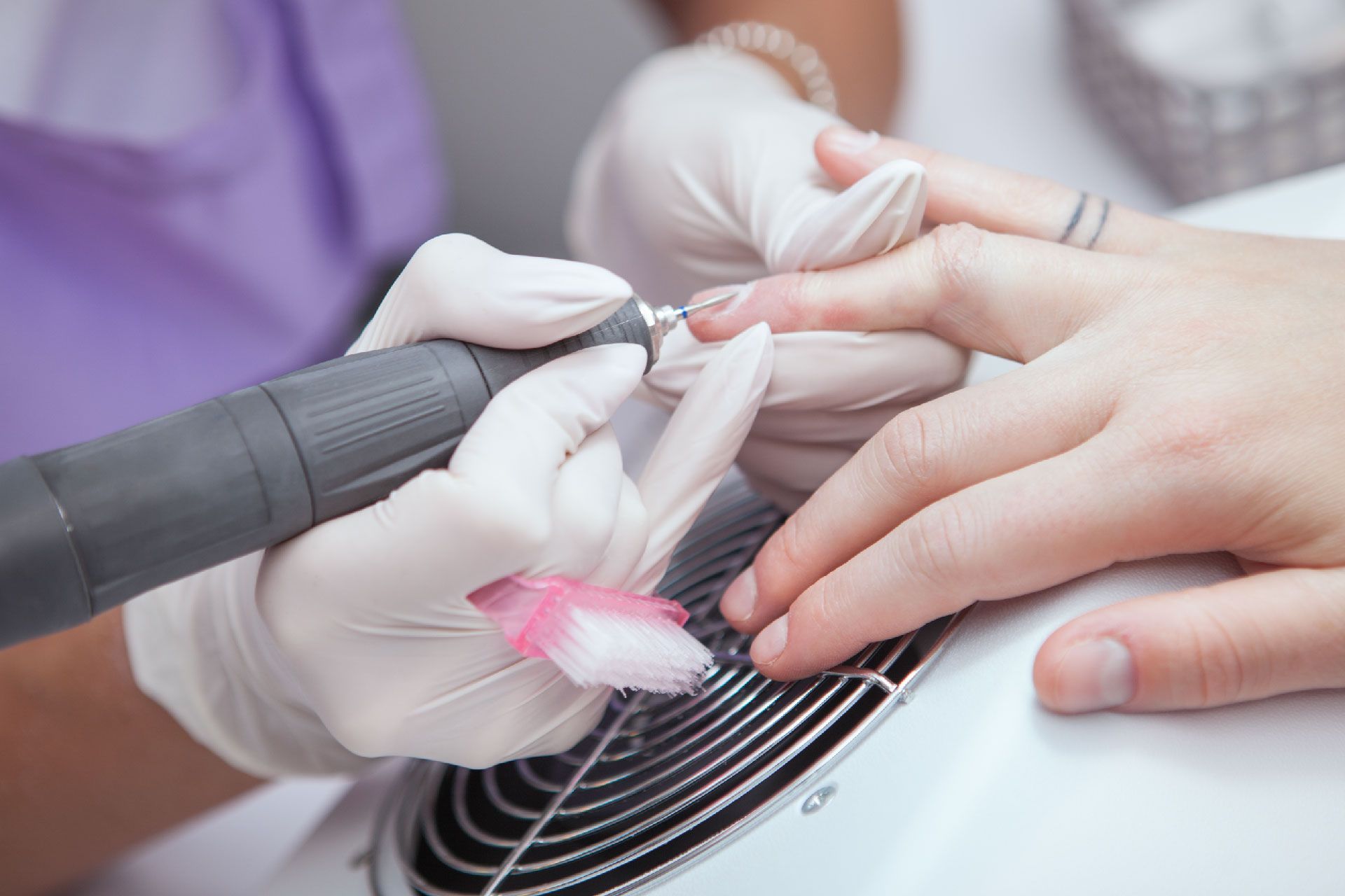 Manicurista limando la uña de una persona con una lima eléctrica, primer plano.