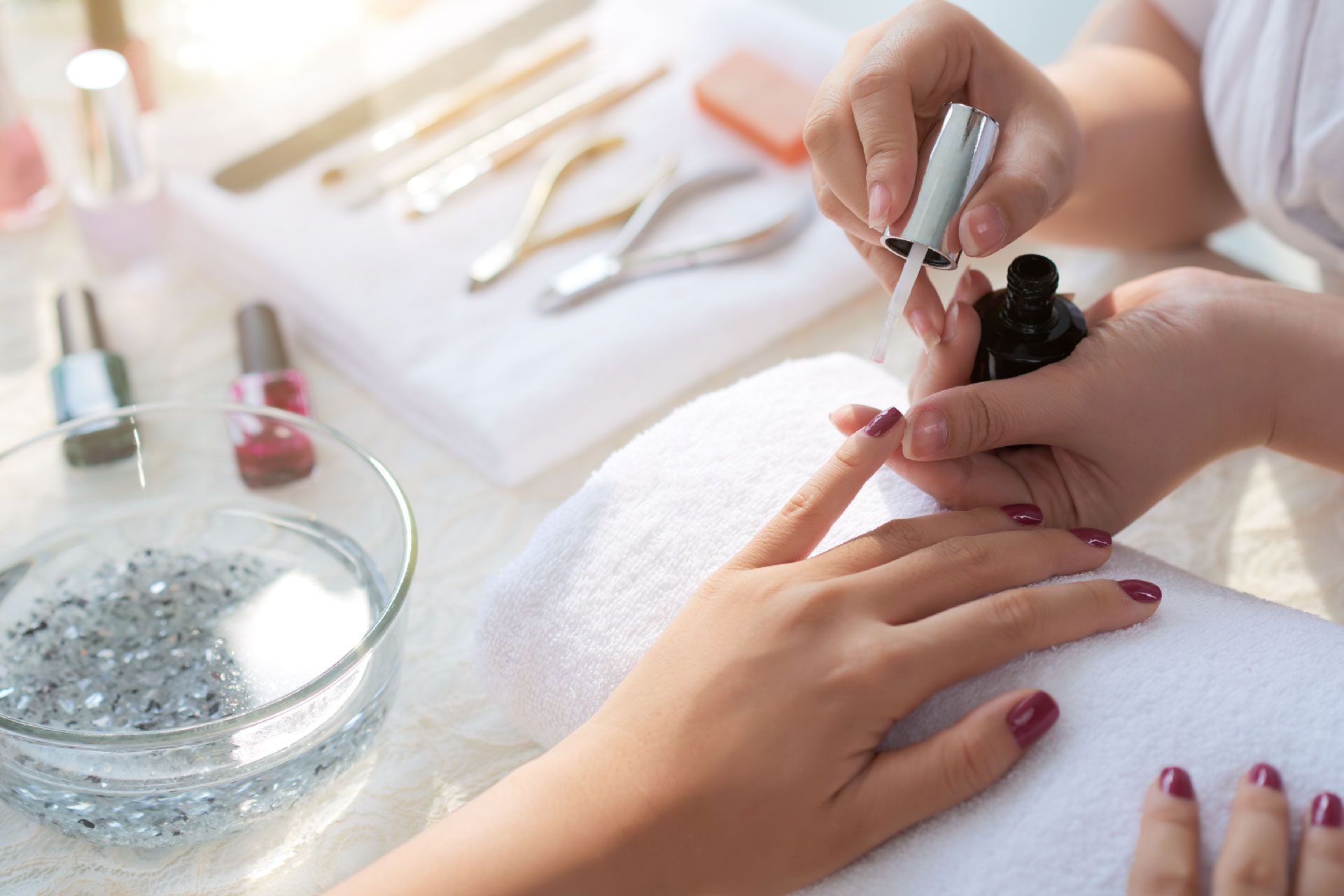 Manicurista aplicando esmalte de uñas rojo en la uña de una clienta, entorno de salón.