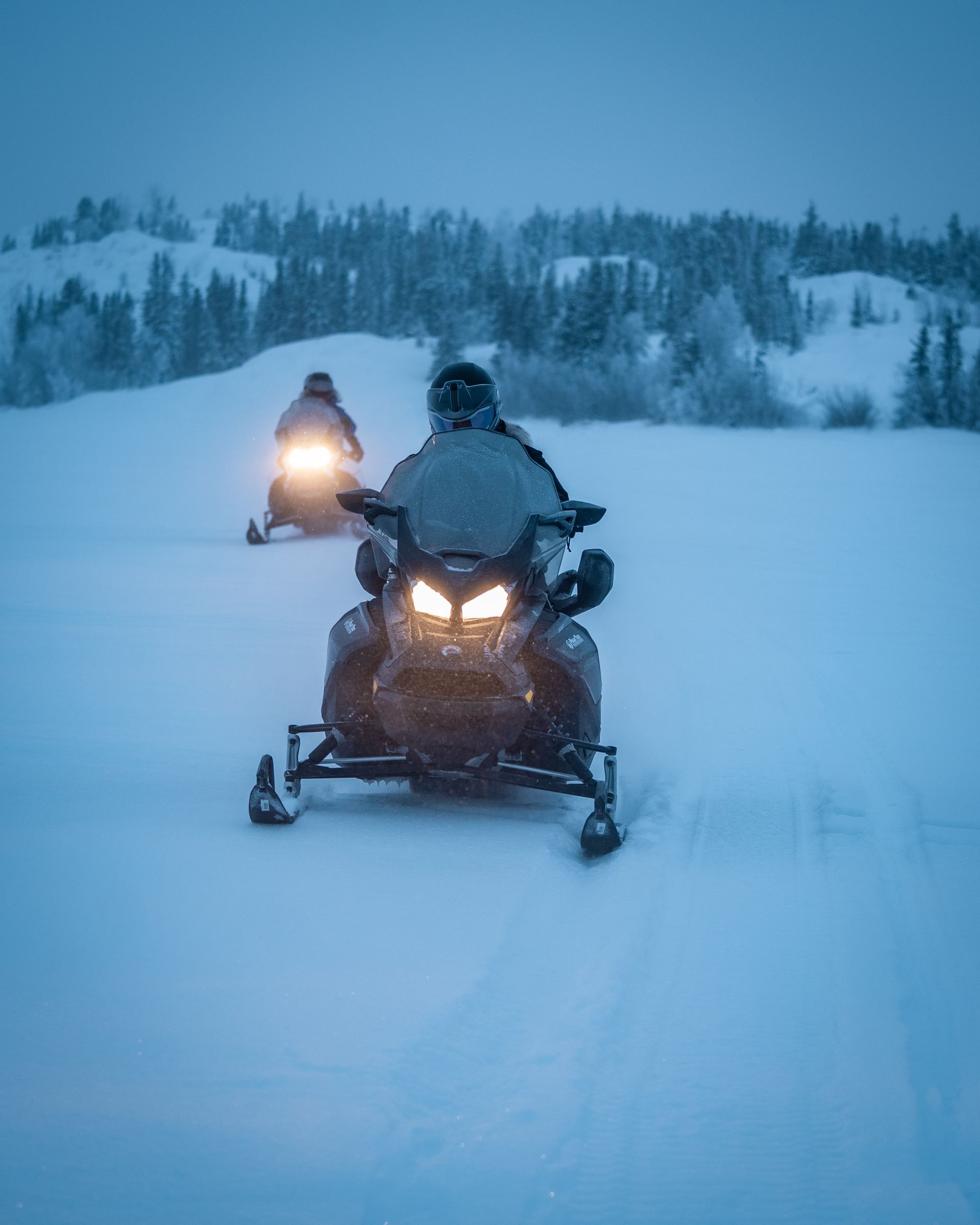 Two people are riding snowmobiles in the snow.