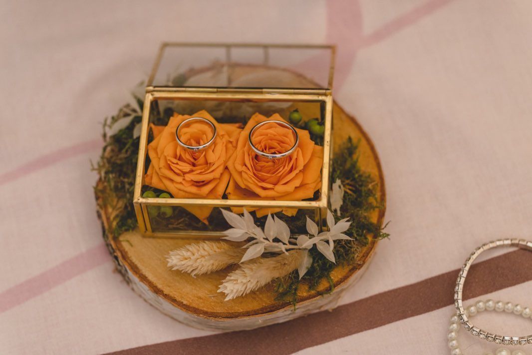 anelli in una scatola di vetro con rose arancioni.