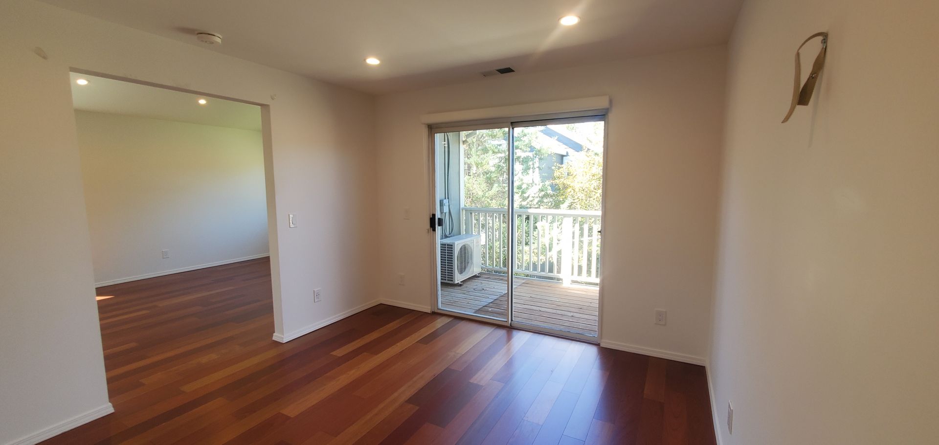An empty living room with hardwood floors and a sliding glass door leading to a balcony.