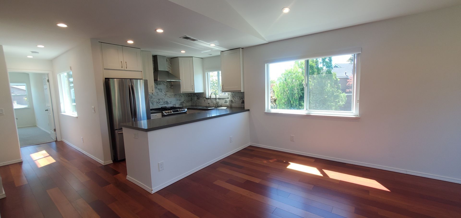 A living room with hardwood floors and a kitchen in the background.