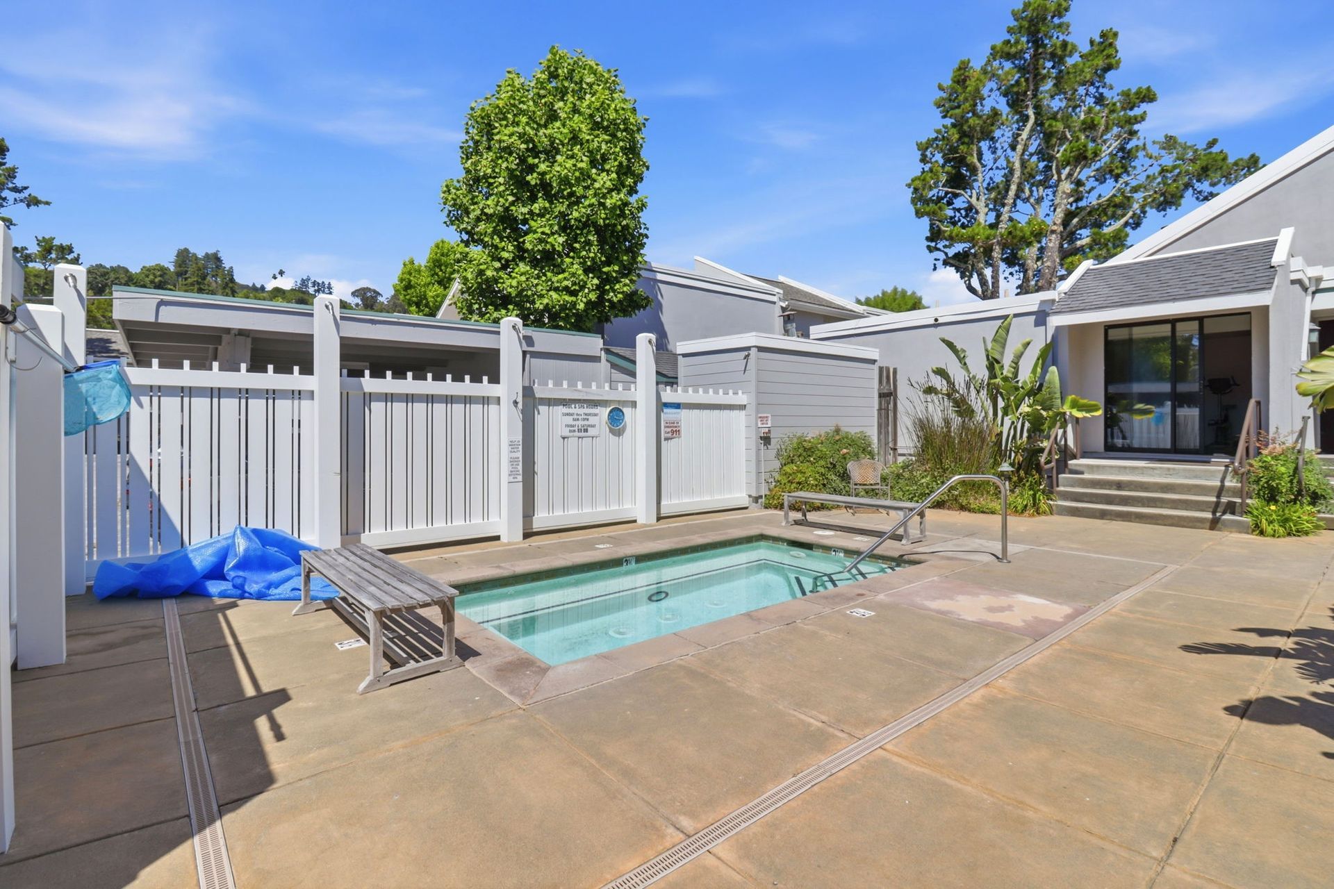 Backyard patio with a small rectangular pool, white fence, and lounge chair under a sunny sky