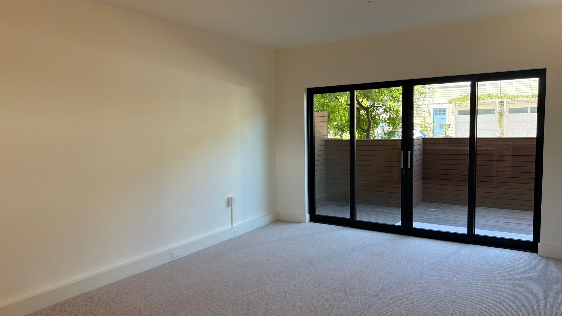 Empty room with beige walls and carpet, a sliding glass door, and outdoor view.
