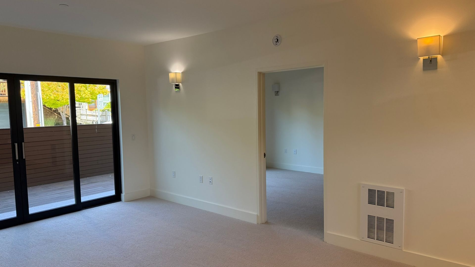 Empty room with sliding glass door, two sconces, and doorway; neutral colors.