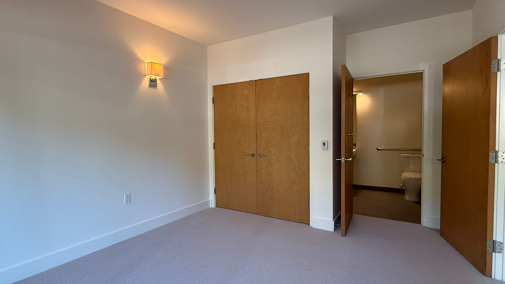 Empty bedroom with beige carpet, closet, and bathroom door open.