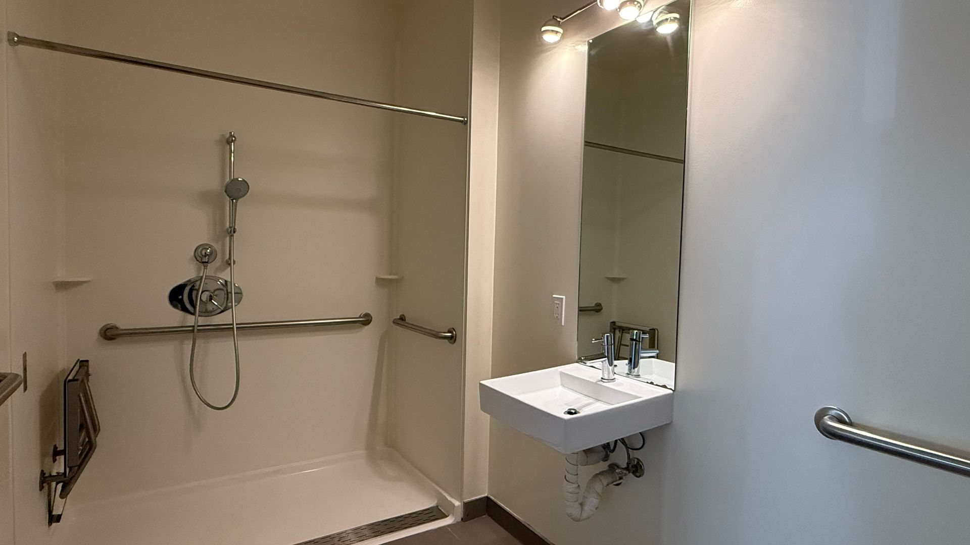 Accessible bathroom with shower, sink, grab bars. White walls, silver fixtures.
