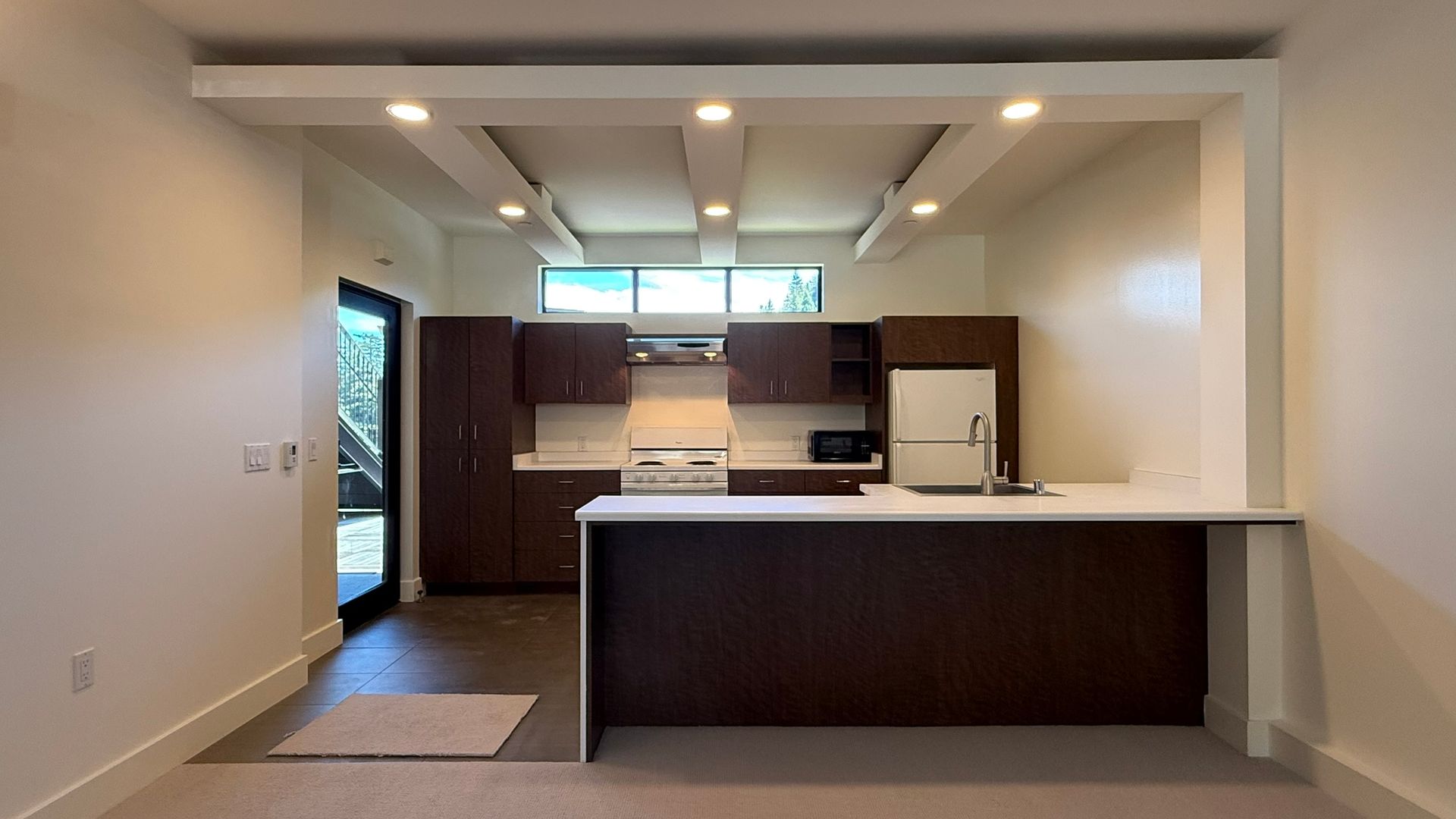 Modern kitchen with dark cabinets, white countertops, and a breakfast bar, under a light-filled ceiling.