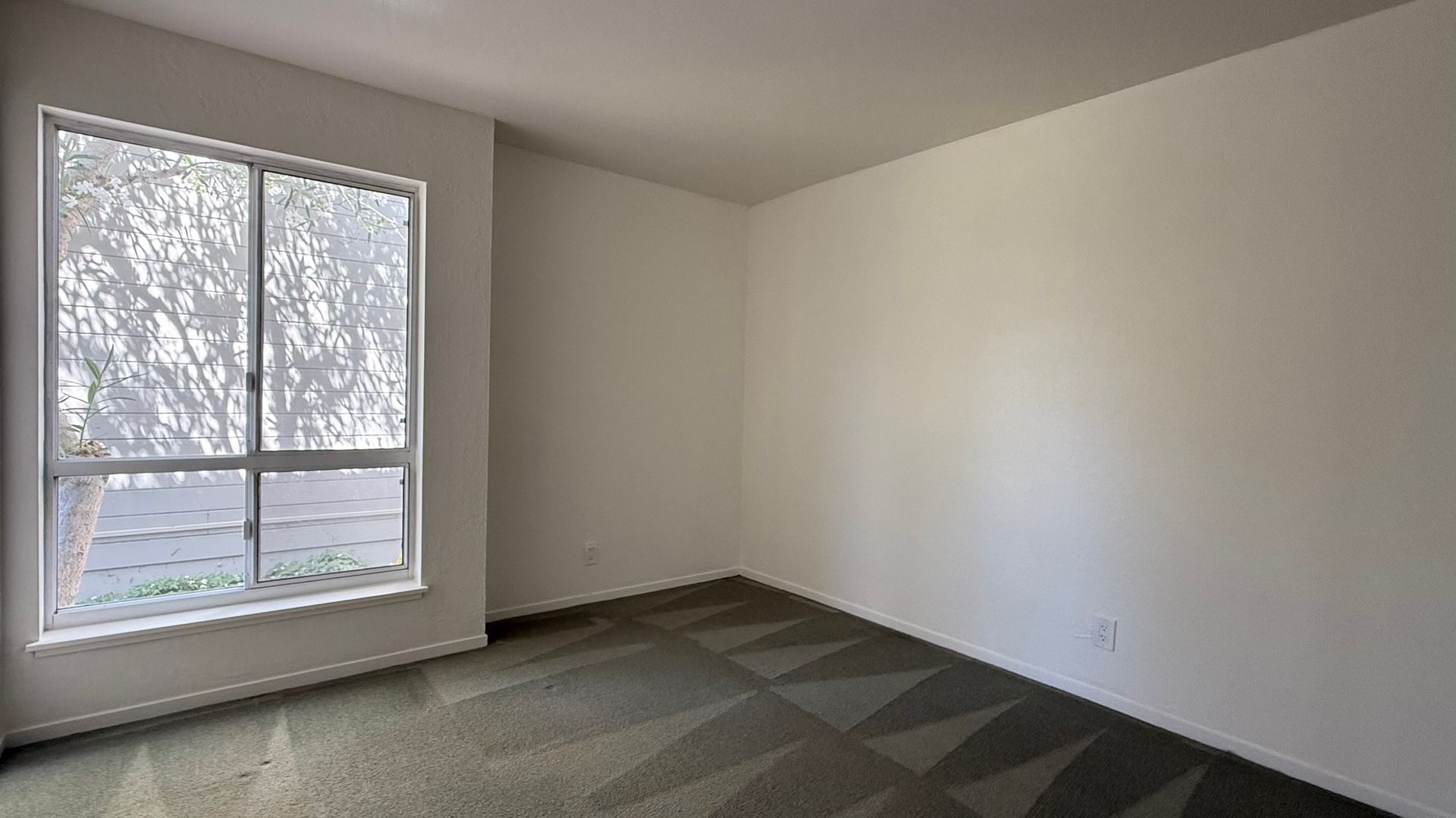 Empty room with a large window and patterned carpet.
