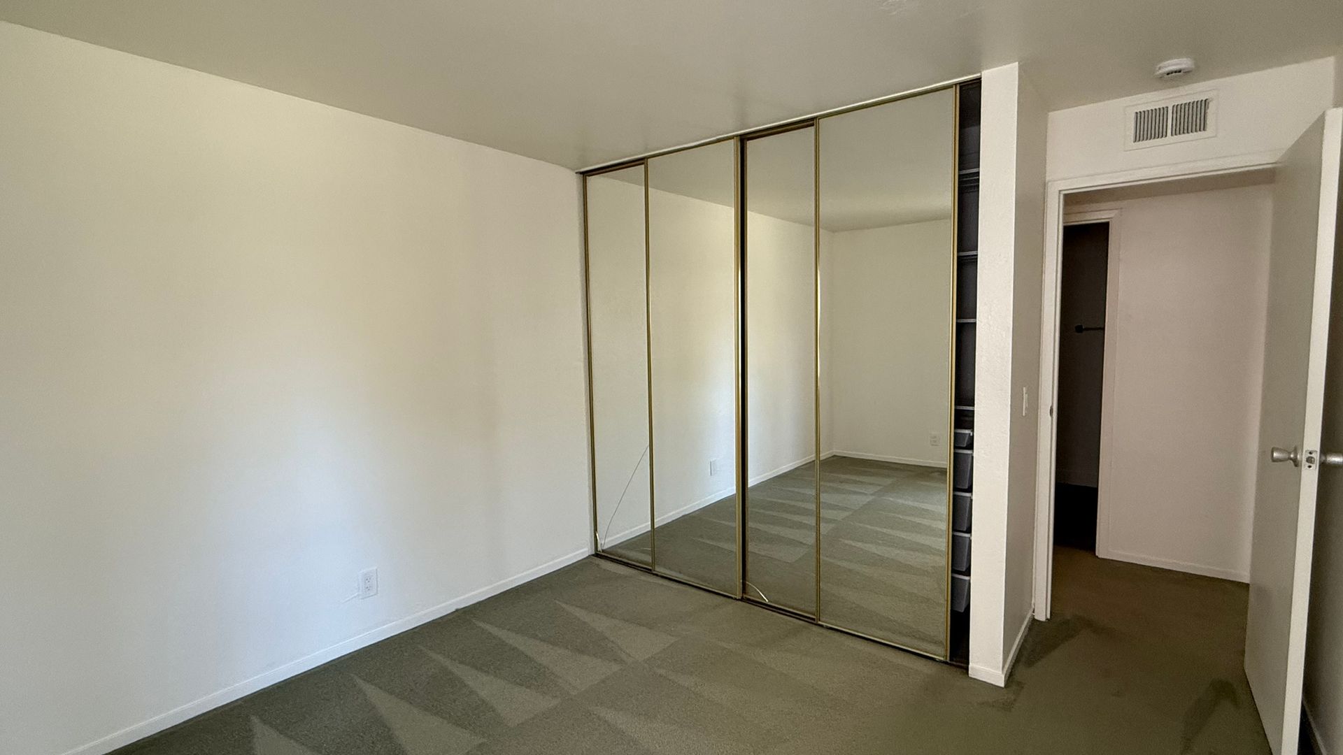 Empty bedroom with mirrored closet doors, carpet, and open doorway.