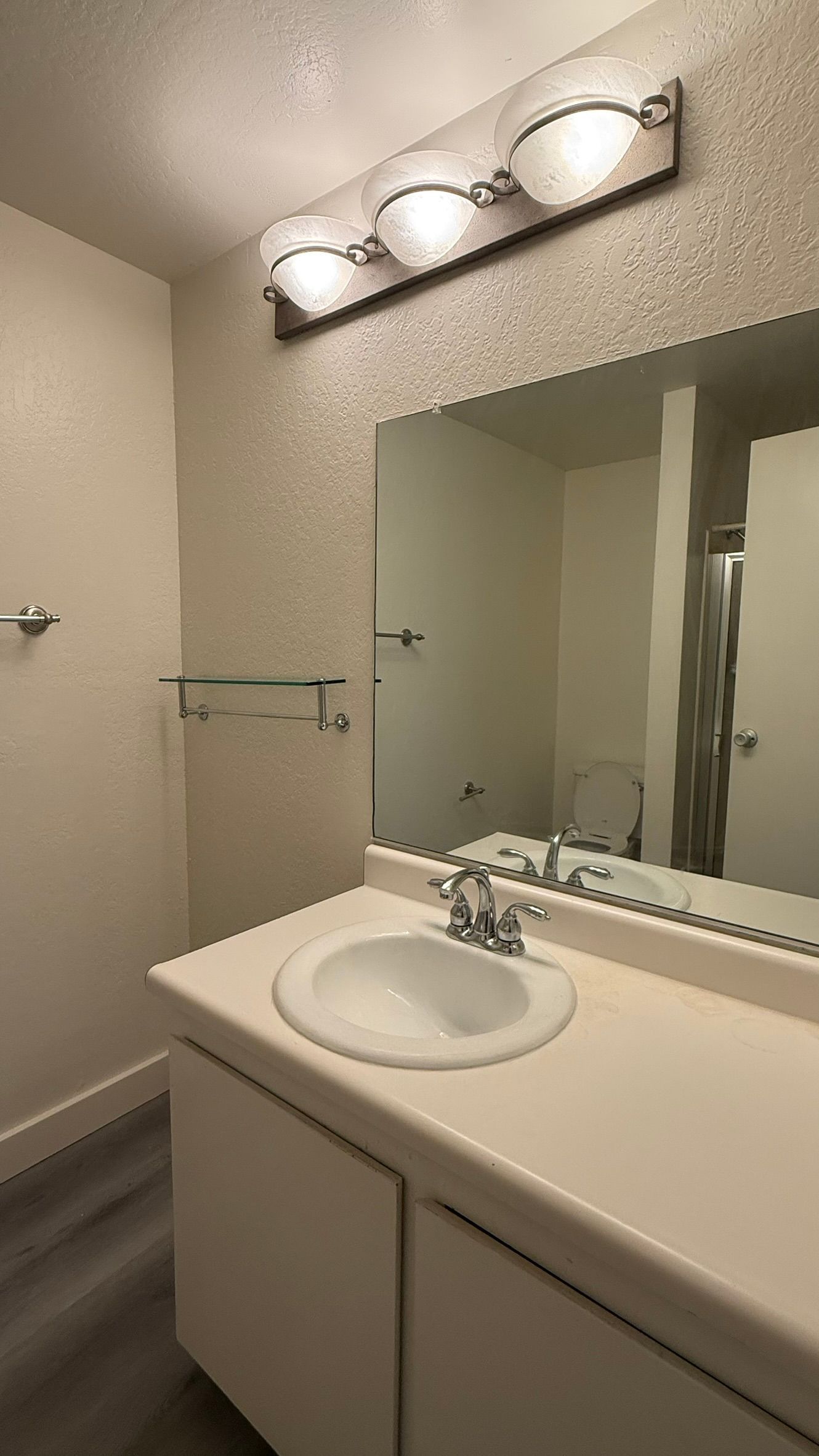 Bathroom with a sink, mirror, and a three-light fixture. Beige and white tones.