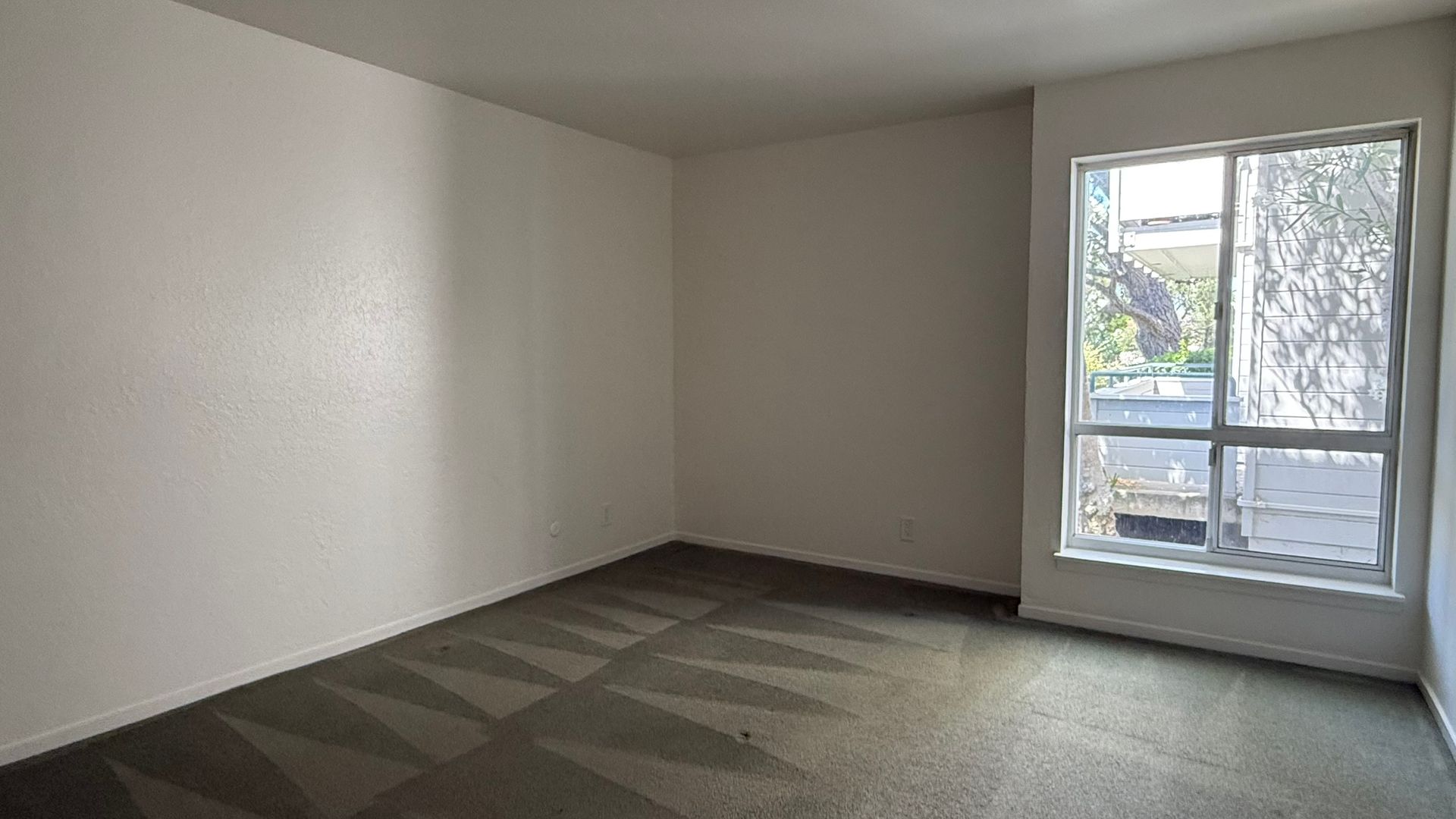 Empty room with off-white walls, a window, and a patterned carpet in a grayscale color scheme.