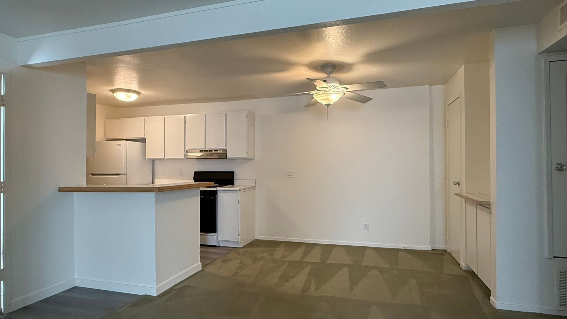 White-walled apartment with an open kitchen featuring white cabinets and a breakfast bar.